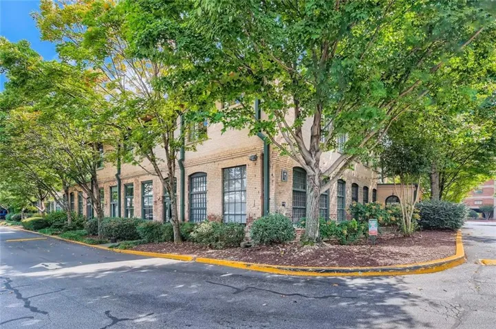 Brick exterior building with multiple windows, surrounded by mature trees and landscaping