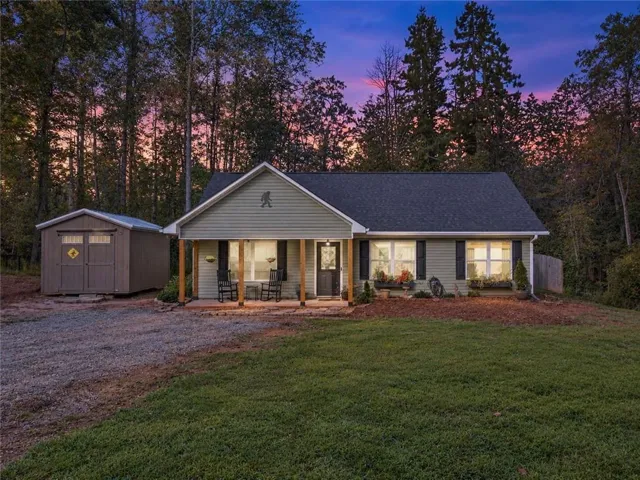 Single-story residence featuring light-colored siding, a dark-toned roof, and a front porch with wooden support posts
