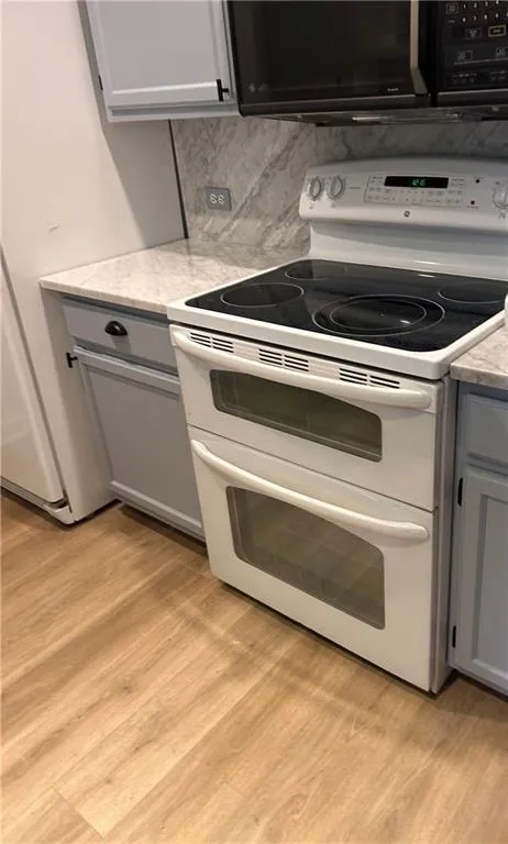 Kitchen featuring light hardwood / wood-style flooring, gray cabinetry, double oven range, light stone counters, and decorative backsplash