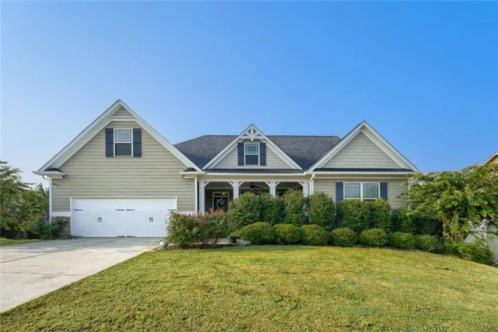 Craftsman-style home featuring a covered front porch, a two-car garage with carriage-style doors, and dormer windows with dark shutters