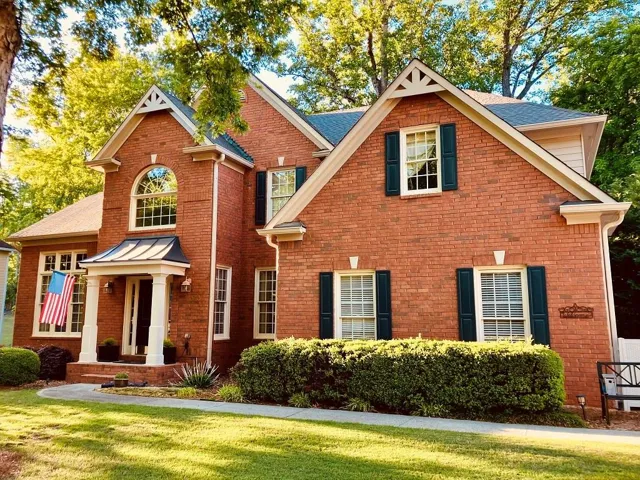 Beautiful Brick "Southwick" floor plan  featuring a covered front entry with columns, arch-top window, dark shutters, and a manicured shrub line - New exterior paint!