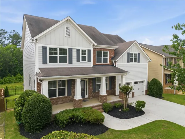 Two-story residence featuring a covered front porch with column supports, brick and siding exterior, attached two-car garage, and a concrete driveway