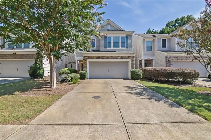 Siding exterior with stone accents, attached garage, concrete driveway, and landscaped shrubbery