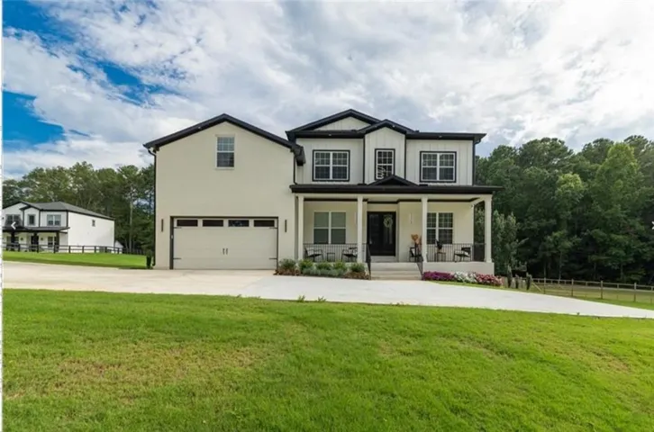 Two-story exterior with white siding and black trim, covered front porch, attached two-car garage, expansive concrete driveway, and a sloped lawn