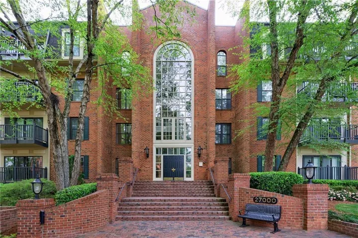 Brick-clad exterior featuring multiple balconies, a grand arched window, and a prominent entrance with brick-paver steps