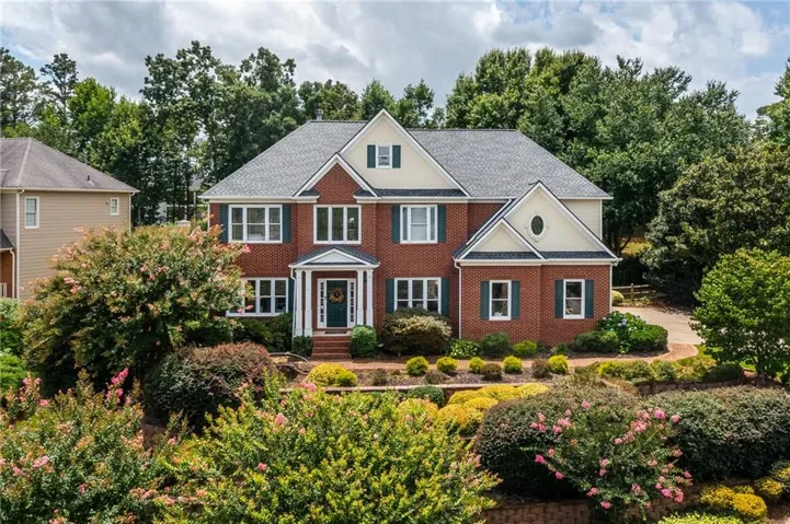 Traditional brick exterior featuring white trim accents, dark green shutters, and a prominent front entry with a portico