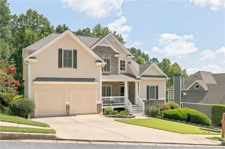 Two-car garage with panel detailing, stone facade accents, covered front porch with white railing, and gabled rooflines