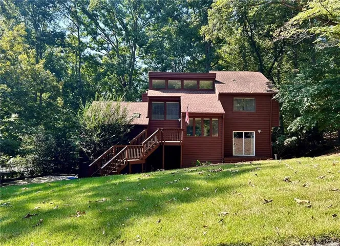 Multi-level exterior with rich red siding, multiple windows, and a prominent deck featuring wood railings