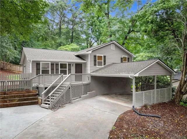 Exterior featuring light gray siding, dark shutters, an elevated wooden deck with railings, an attached carport, and a concrete driveway