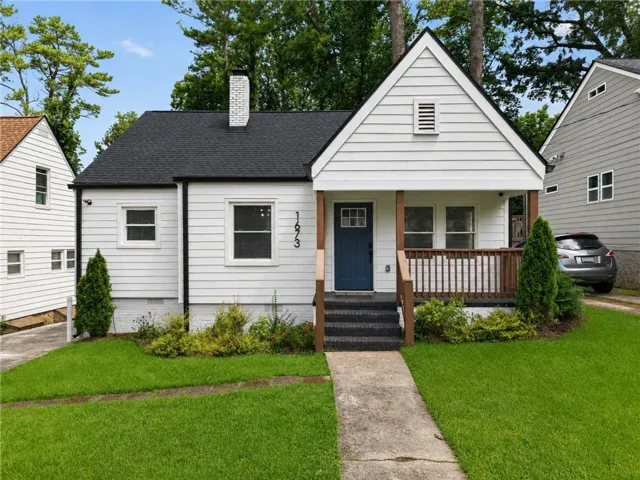 Charming cottage-style home featuring white horizontal siding, a peaked gable roof with dark asphalt shingles, and a welcoming front porch with wooden railings