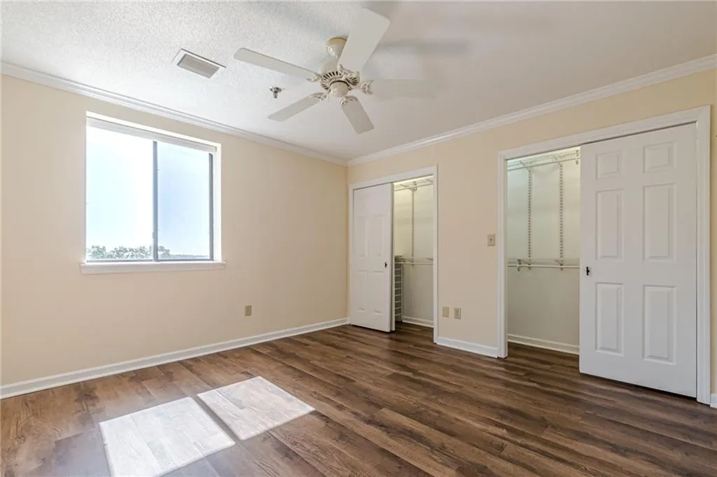 Unfurnished bedroom featuring a textured ceiling, multiple closets, ceiling fan, ornamental molding, and dark hardwood / wood-style floors