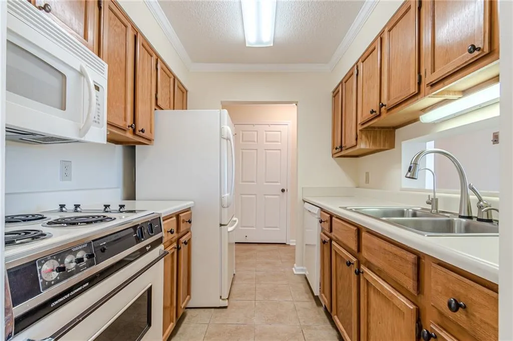 Kitchen with crown molding, a textured ceiling, sink, and white appliances