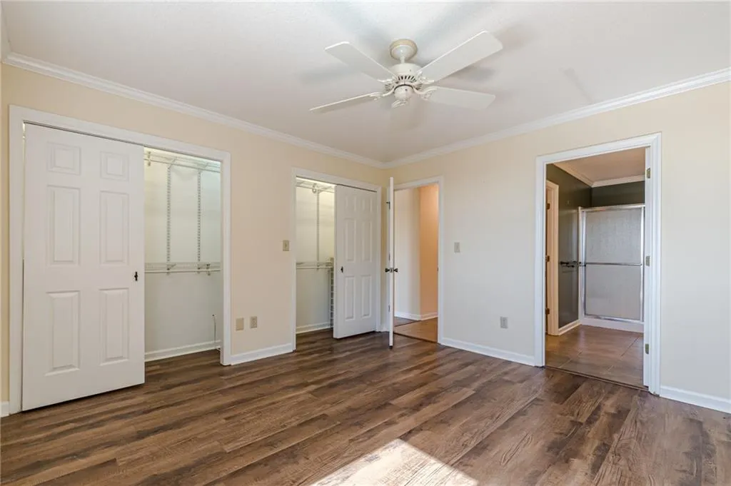 Unfurnished bedroom featuring ornamental molding, two closets, dark hardwood / wood-style floors, and ceiling fan