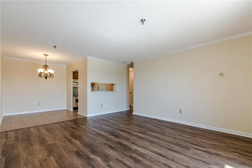 Unfurnished living room featuring a notable chandelier, dark wood-type flooring, and crown molding