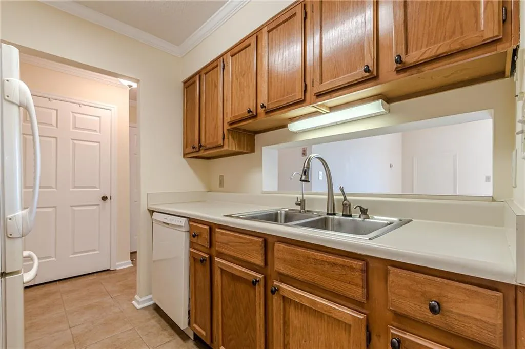 Kitchen with white appliances, crown molding, light tile patterned flooring, and sink
