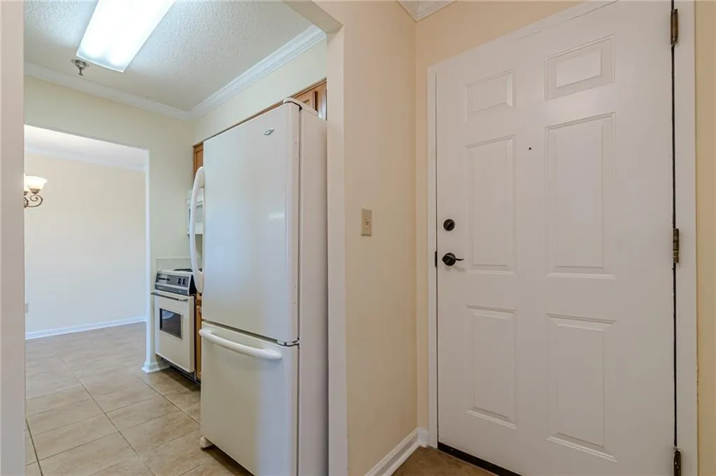Kitchen featuring crown molding, a textured ceiling, white appliances, and light tile patterned floors