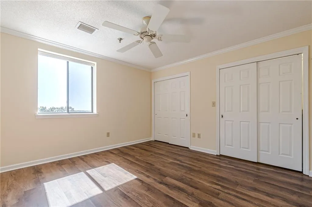 Unfurnished bedroom featuring crown molding, two closets, dark hardwood / wood-style floors, and ceiling fan