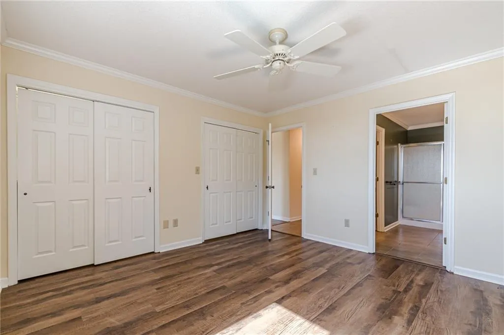 Unfurnished bedroom featuring ornamental molding, two closets, dark wood-type flooring, and ceiling fan