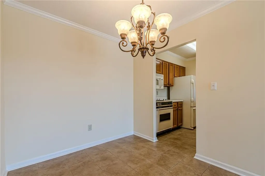Kitchen featuring white appliances, light tile patterned flooring, hanging light fixtures, crown molding, and a chandelier