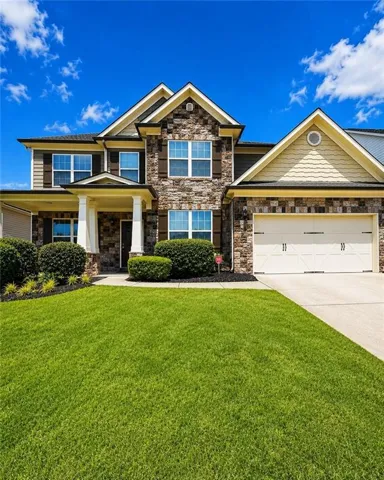 Stone and siding exterior featuring a two-car garage, covered porch entry, and a vibrant green lawn