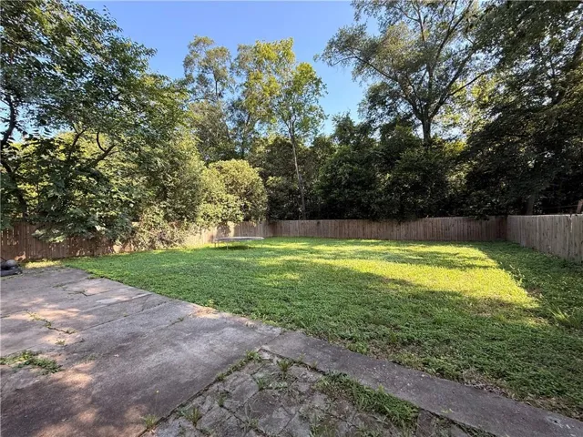 Expansive rear yard featuring a wooden privacy fence, mature perimeter trees, a concrete patio, and a grass lawn