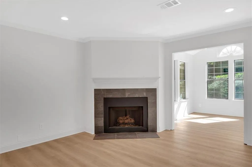 Unfurnished living room with ornamental molding, a tiled fireplace, and light hardwood / wood-style floors