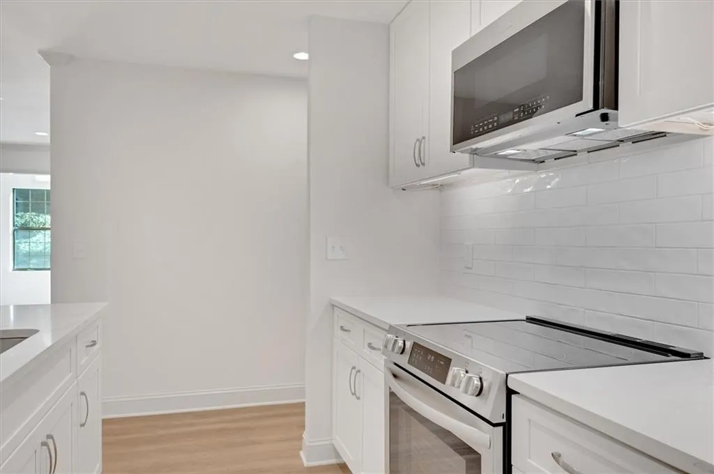 Kitchen with light wood-type flooring, white cabinetry, stainless steel appliances, and backsplash