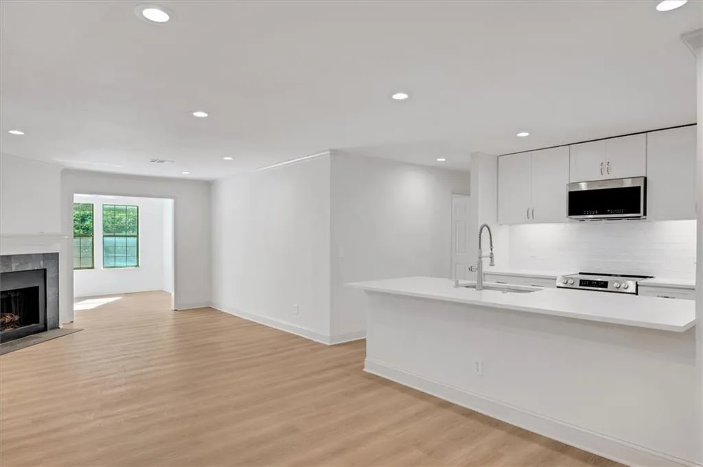 Kitchen with sink, a tiled fireplace, white cabinetry, appliances with stainless steel finishes, and light wood-type flooring