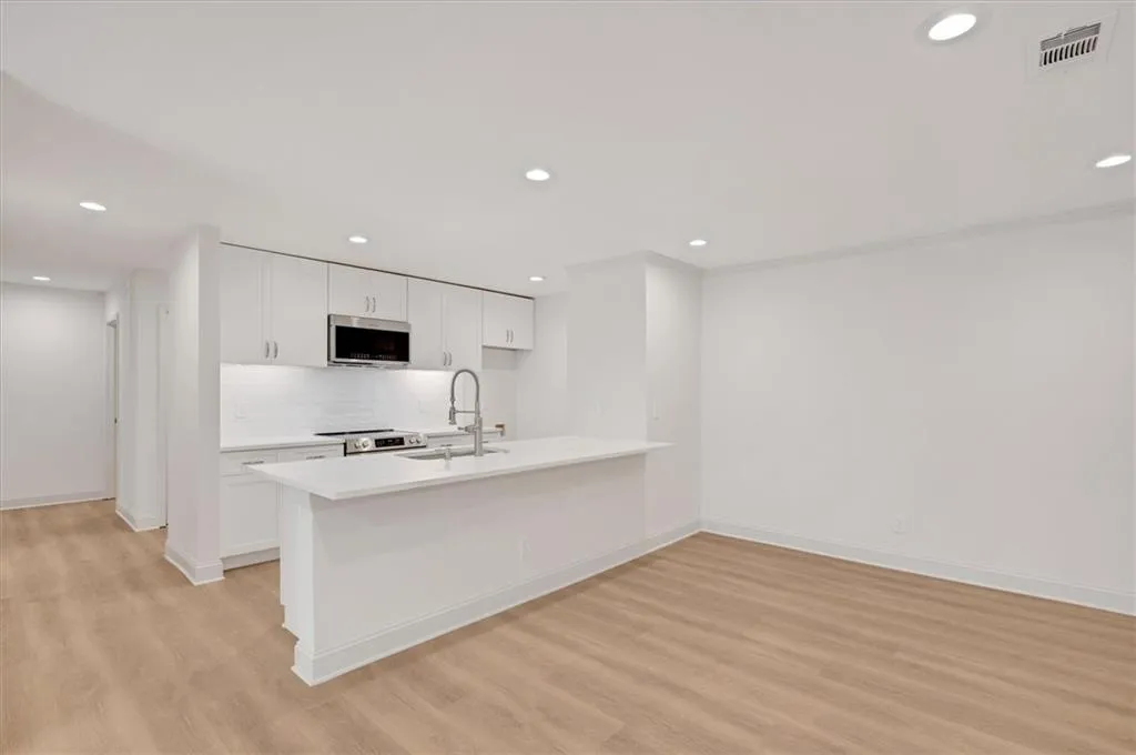 Kitchen with appliances with stainless steel finishes, light wood-type flooring, sink, and white cabinetry