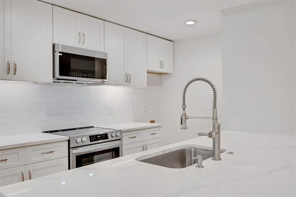Kitchen featuring stainless steel appliances, light stone countertops, white cabinets, and sink