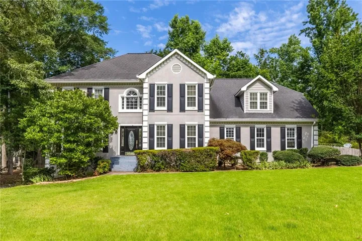 Two-story stucco residence featuring a central arched window, black louvered shutters, a dark panel front door with decorative glass, and a dormer window