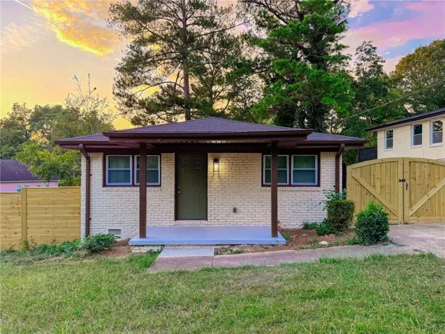 Brick exterior with covered front porch, dark-framed windows, wood fencing, and a wood gate