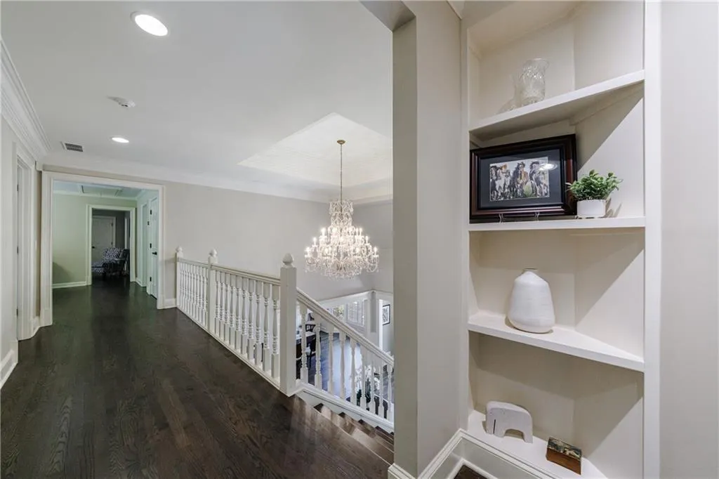 Corridor featuring a chandelier, built in features, dark hardwood  floors, wide hallway and crown molding