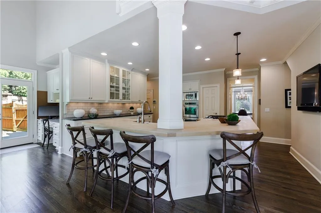 Kitchen featuring white cabinetry, decorative columns, appliances with stainless steel finishes, a kitchen bar, and tasteful backsplash