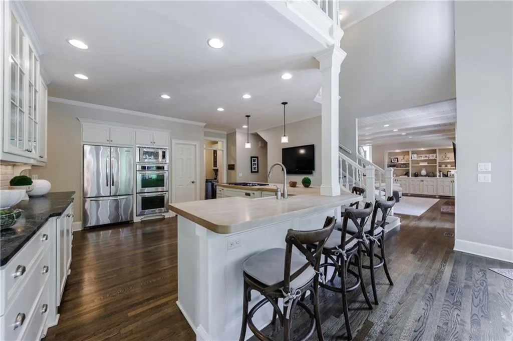 Kitchen featuring built in appliances, a kitchen breakfast bar, hanging light fixtures, dark hardwood flooring, and white cabinetry