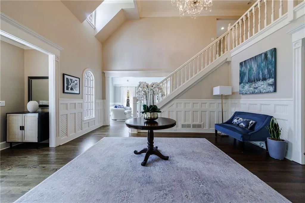 Entry foyer looking into living room hardwood flooring, a notable chandelier, and a high ceiling