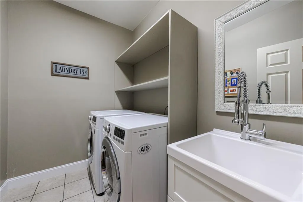 Laundry area with light tile floors, washing machine and clothes dryer, and sink