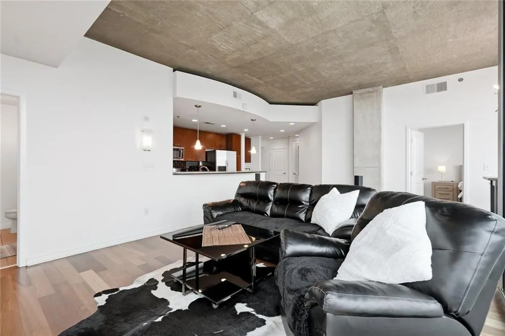 Open-concept living area featuring a concrete ceiling, wood-finish flooring, and a kitchen pass-through with pendant lighting