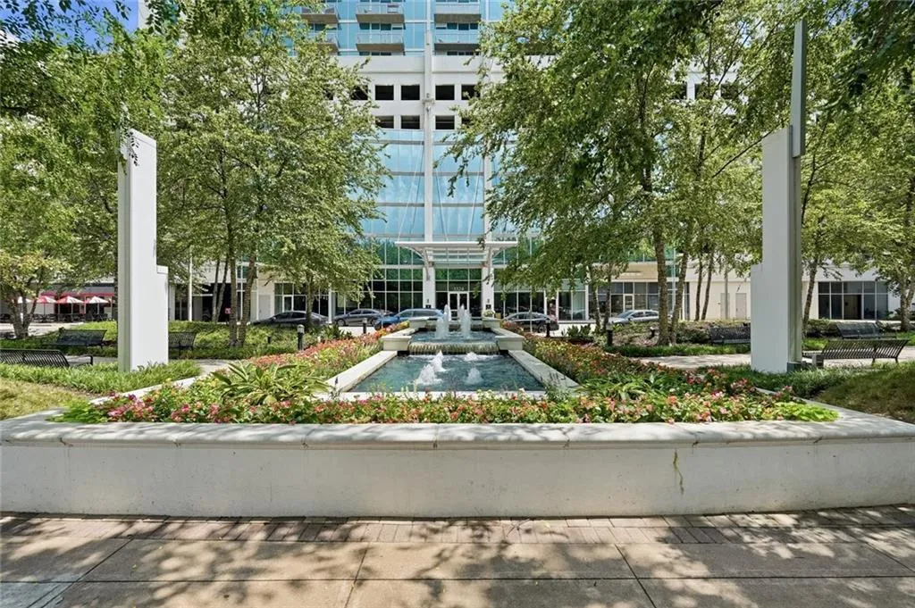 Modern building entrance featuring a water fountain, established landscaping, and mature trees