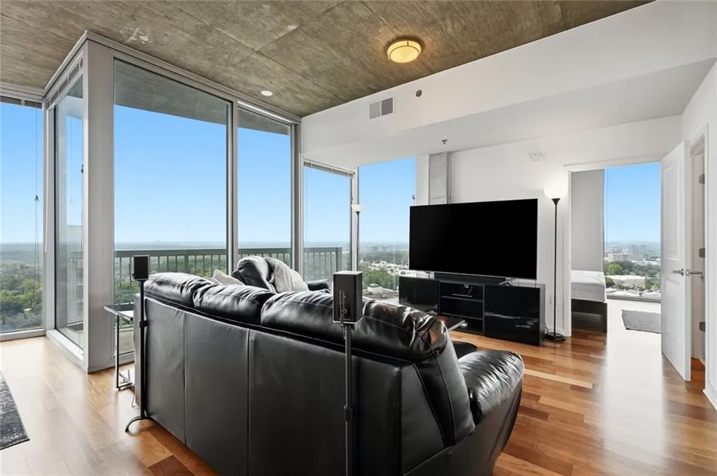 Living area featuring wood-finish flooring, a concrete ceiling, and expansive windows with city and tree canopy scenery