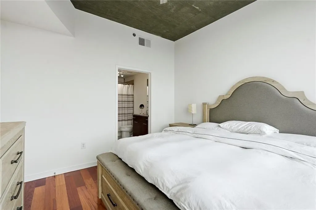 Bedroom featuring wood-finish flooring, a textured ceiling, and a doorway leading to a bathroom with a dark wood vanity and toilet