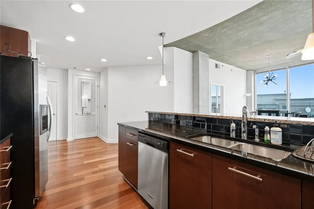 Kitchen featuring dark wood-finish cabinetry, stainless steel appliances, dark granite countertops, and a black subway tile backsplash