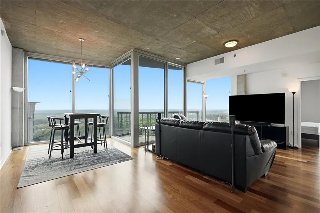 Floor-to-ceiling windows with expansive sky and landscape scenery, featuring hardwood flooring, a concrete ceiling, and a modern chandelier