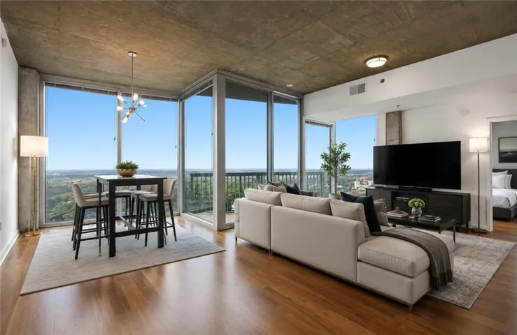 Open-concept living space with expansive floor-to-ceiling windows, wood-finish flooring, and a modern industrial-style ceiling