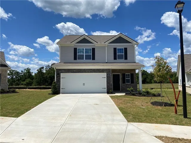 Two-story residence featuring a two-car garage, stone and siding exterior, front porch with columns, and a concrete driveway