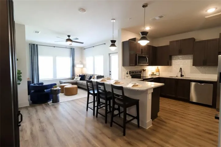 Kitchen with hanging light fixtures, a peninsula, dark brown cabinetry, appliances with stainless steel finishes, and a breakfast bar area