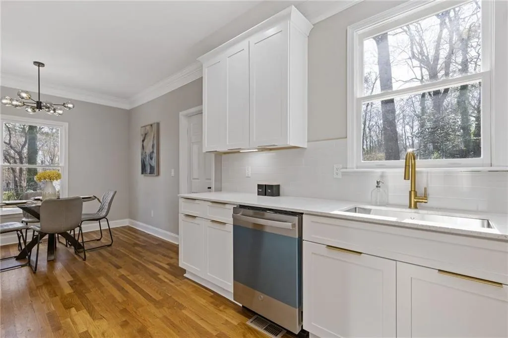 Kitchen with dishwasher, white cabinetry, decorative backsplash, light wood-type flooring, and crown molding