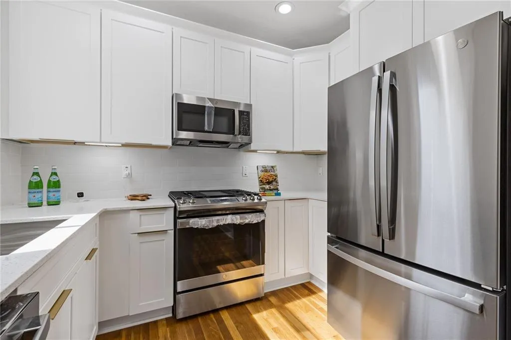 Kitchen with appliances with stainless steel finishes, white cabinetry, light wood-style floors, backsplash, and light stone countertops