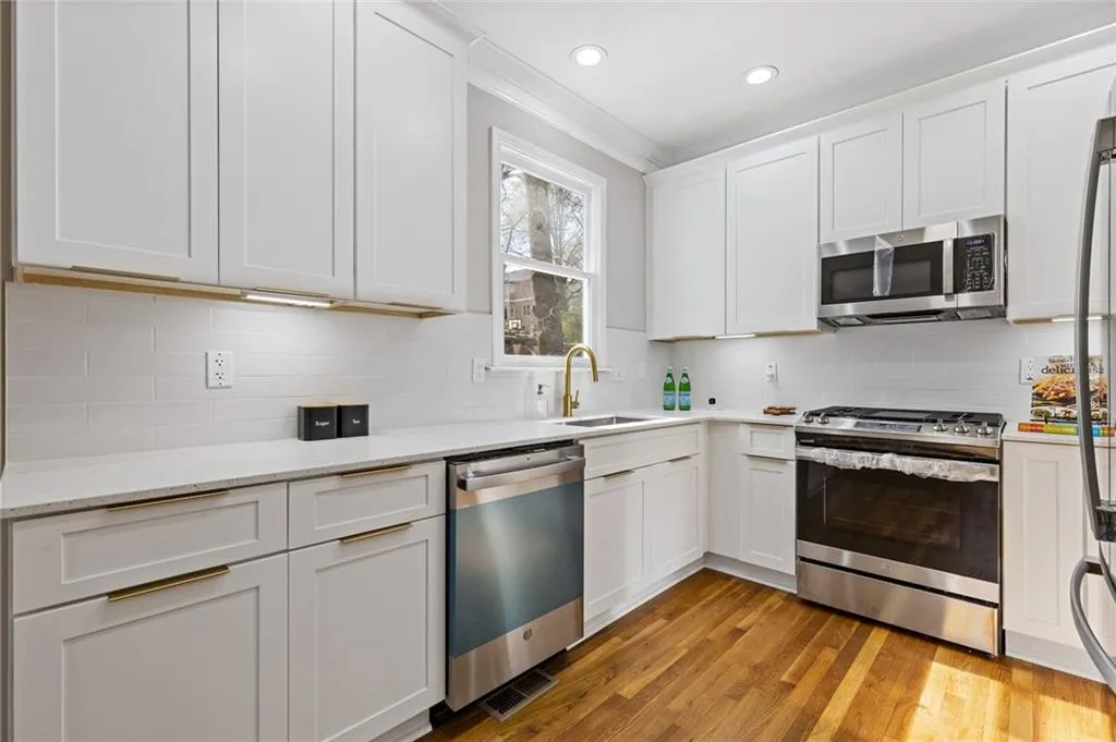 Kitchen featuring stainless steel appliances, white cabinetry, light wood-style floors, decorative backsplash, and light stone counters