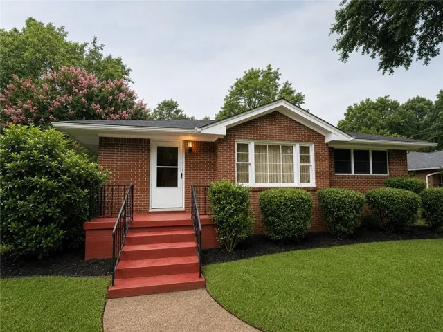 Brick exterior featuring a white entry door, red painted porch and steps, black metal handrails, and mature landscaping